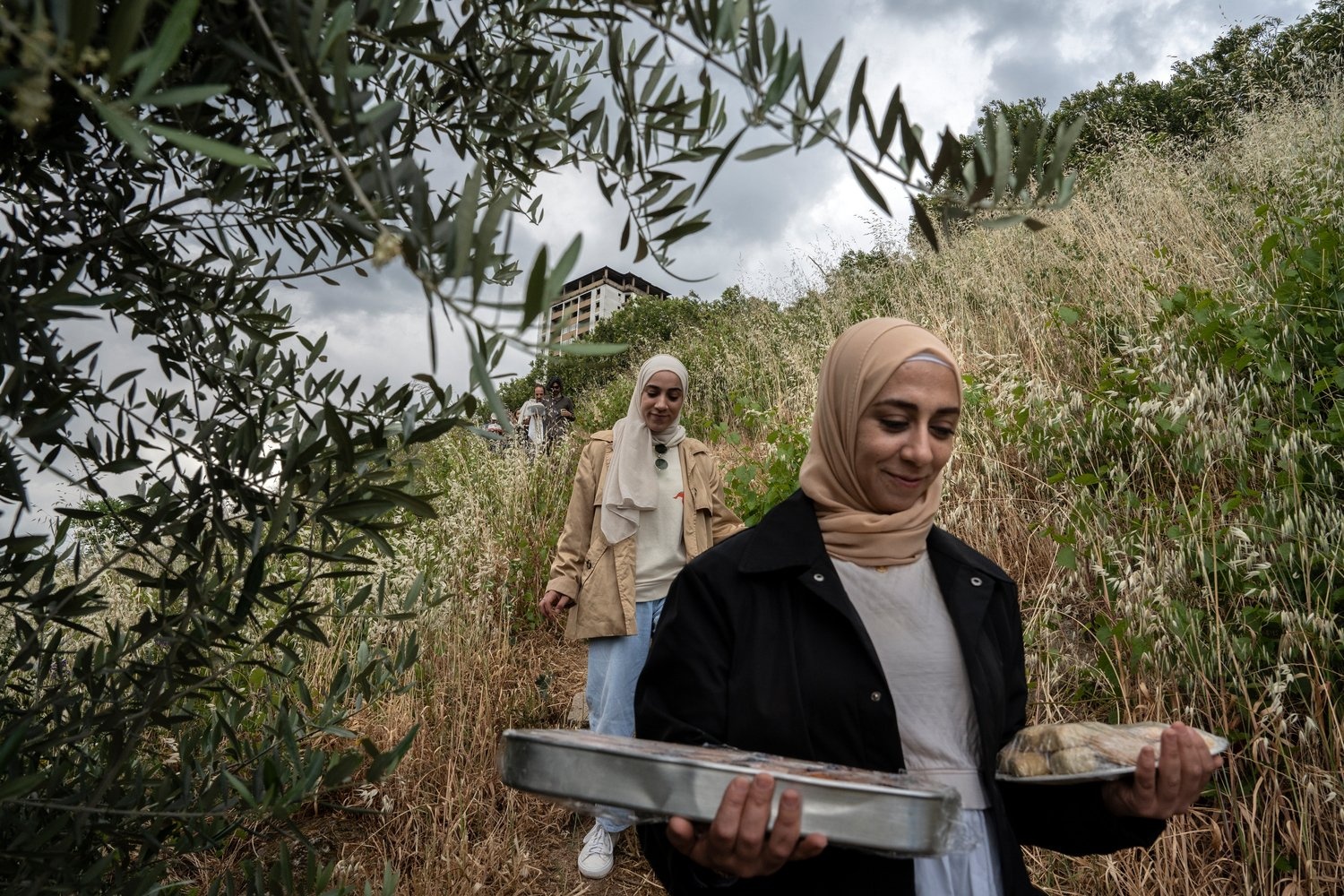 Two sisters carry plates of food down a hillside on their way to a picnic.