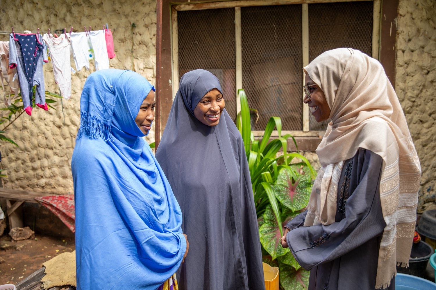 Three smiling women stand together in front of a house.