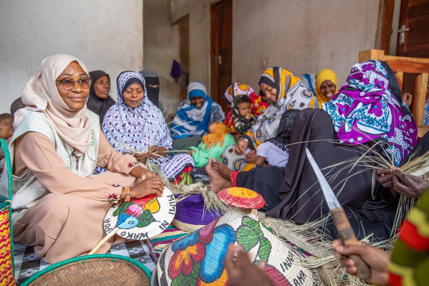 A group of women sit on the floor weaving colourful baskets.