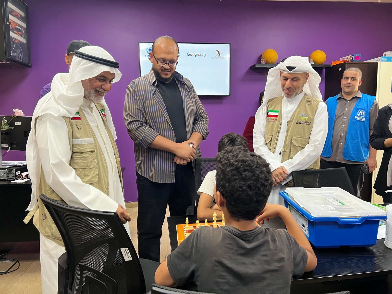 Mr. Jamal standing with adults inside, watching two children play chess