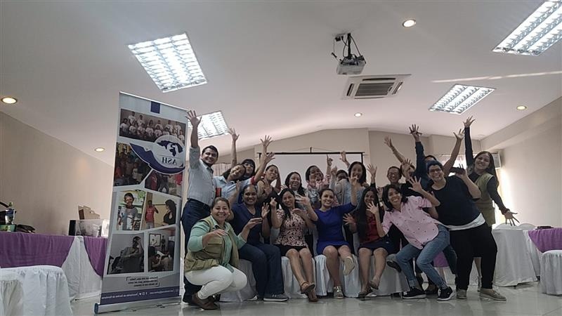 A group of around 20 staff members excitedly pose in a conference room, next to an Asociación de Sordos de Honduras banner