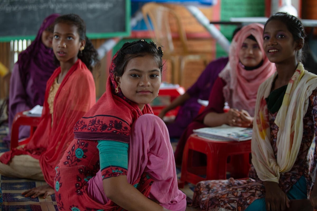 A group of girls wearing colorful clothing sit in a classroom.