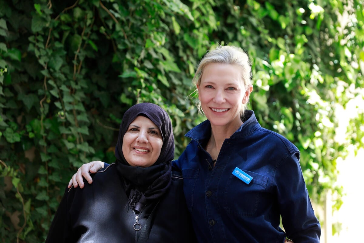 Cate and Yusra Oudeh pose, smiling at the camera, outdoors in front of green foliage