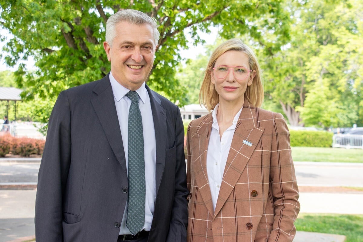 Filippo Grandi and Cate Blanchett stand outside, smiling at the camera, with green trees behind them.