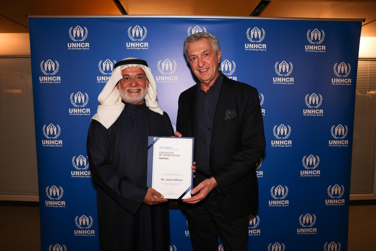 Two smiling men holding a certificate of appreciation, with a UNHCR banner behind them