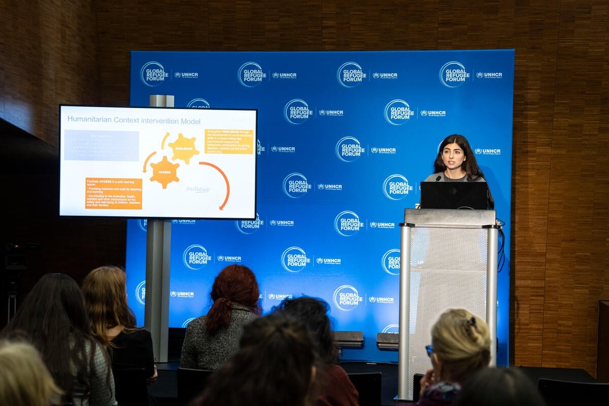A woman at a lectern addresses an audience, with a presentation to her right and a GRF banner behind her