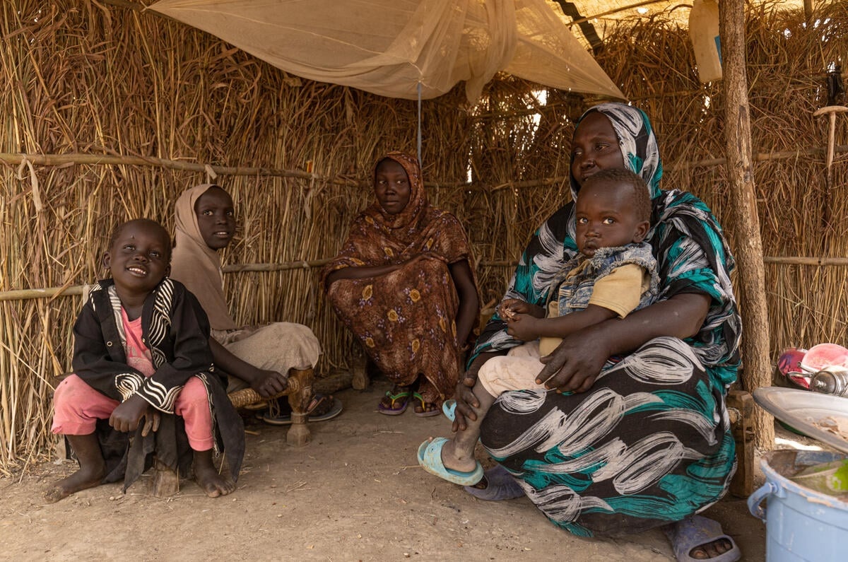 A woman and four children sit smiling inside a shelter
