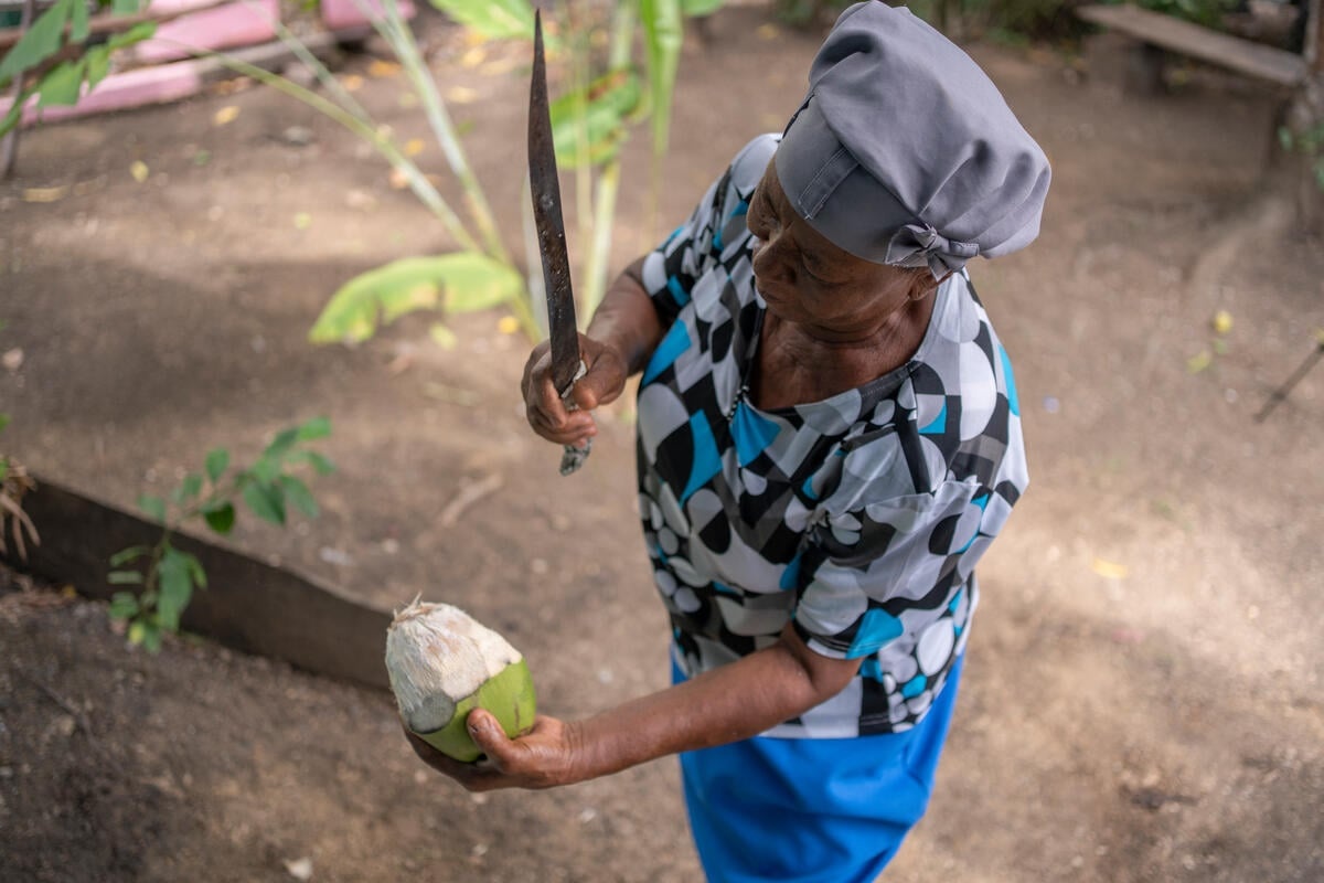A woman filmed from above holds a machete over a coconut in her hand.