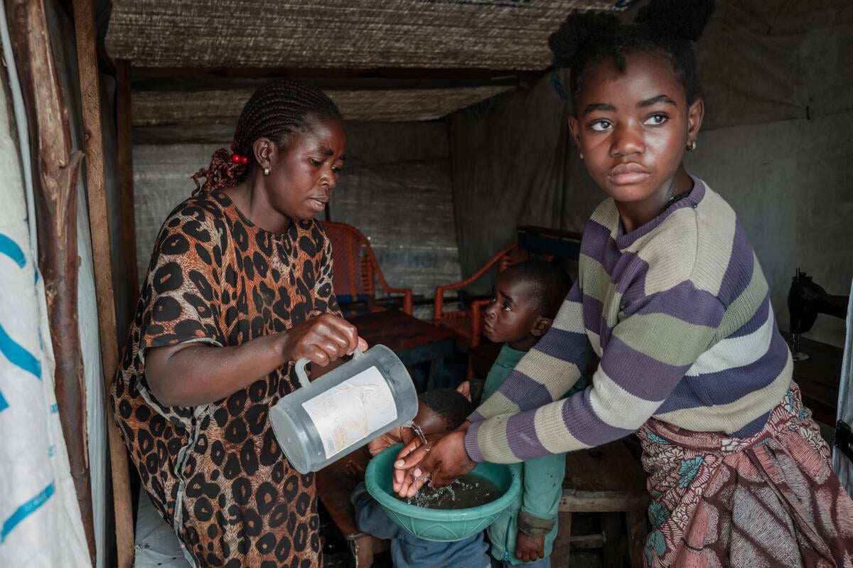 A girl washes her hands in a small basin held by a woman pouring water from a plastic jug.