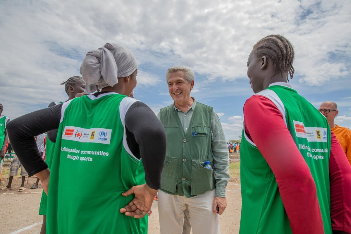 A man in a green vest talks to two young women with their backs to the camera.
