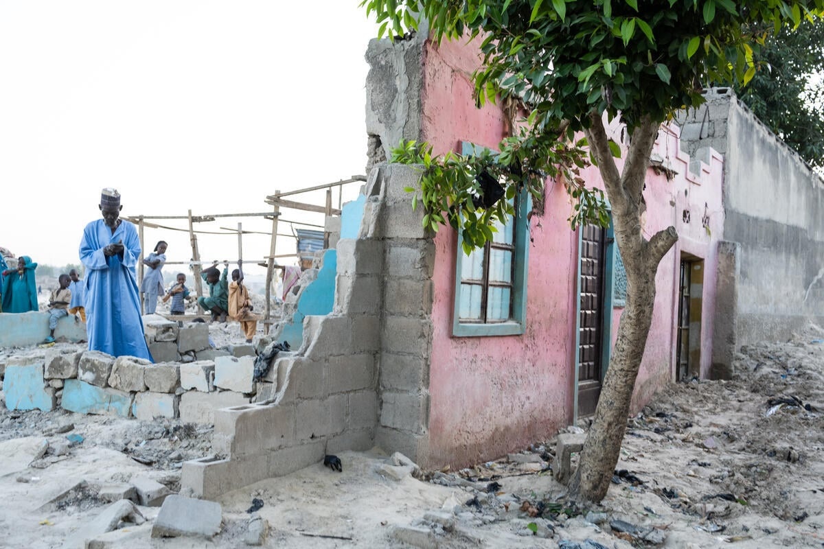 A man stands in the ruins of a house, only the facade of which is still standing.