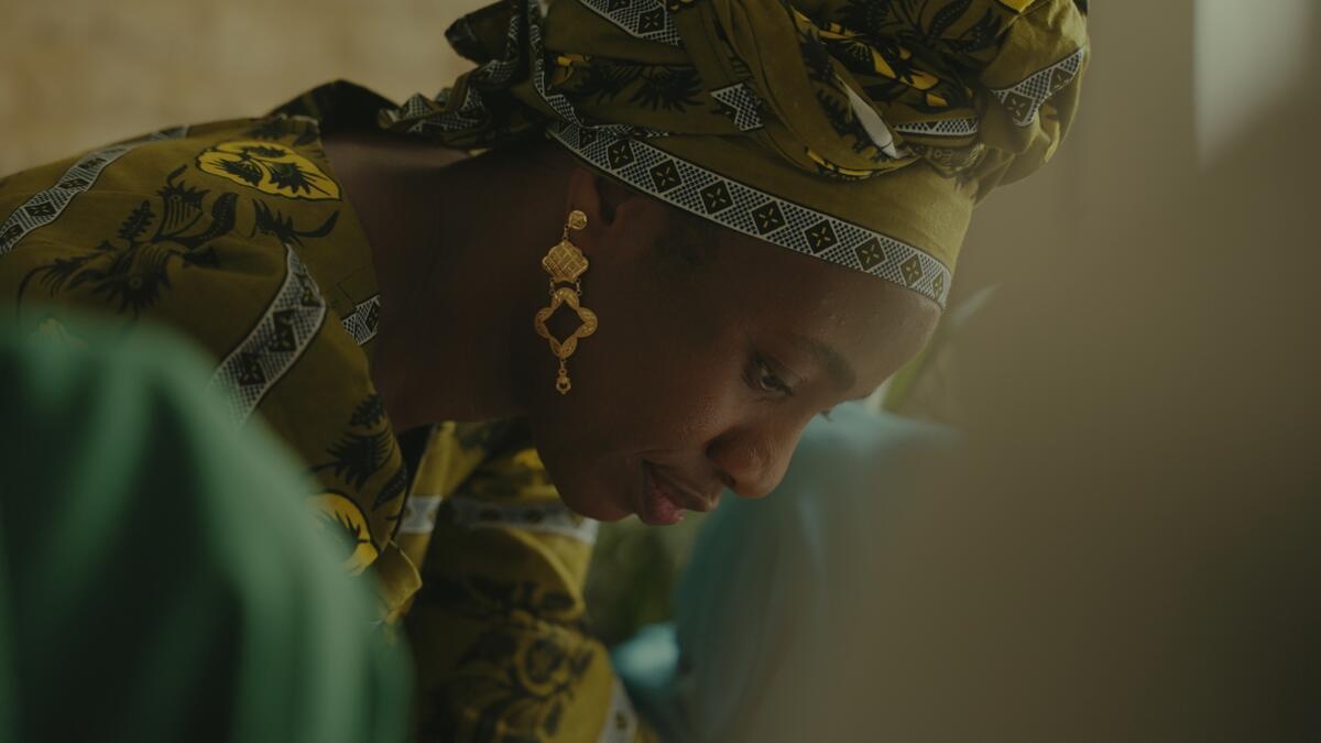 A woman wearing a matching green dress and headscarf leans down to look at something.