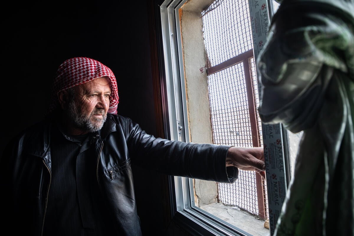 A man in a red headscarf stands beside a window.