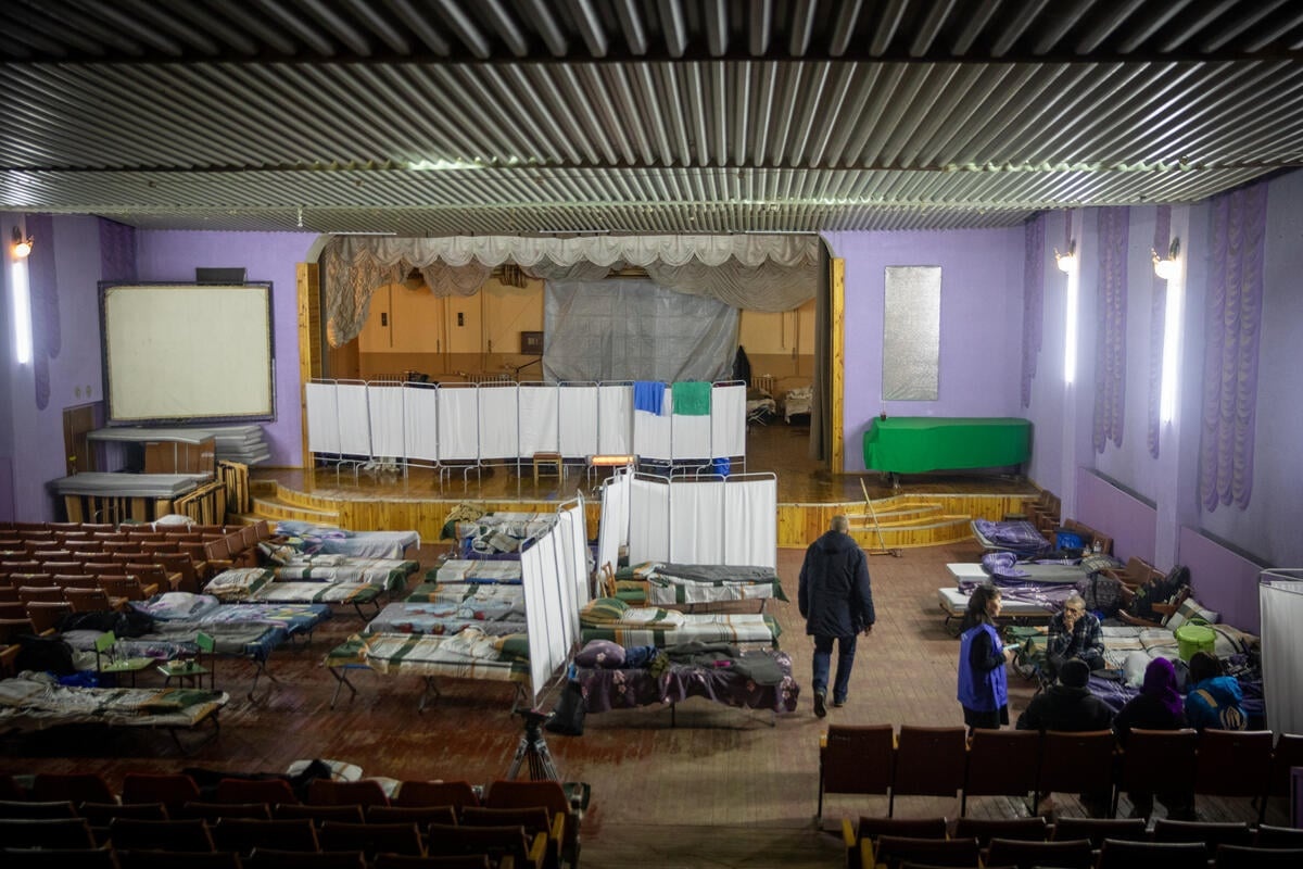 A school hall filled with camp beds and screens dividing them.
