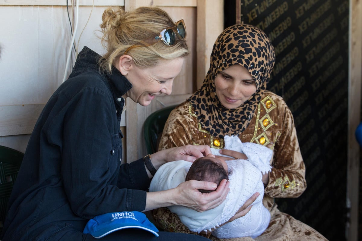 Cate sitting with another woman and her newborn baby, Cate cradling the baby's head.