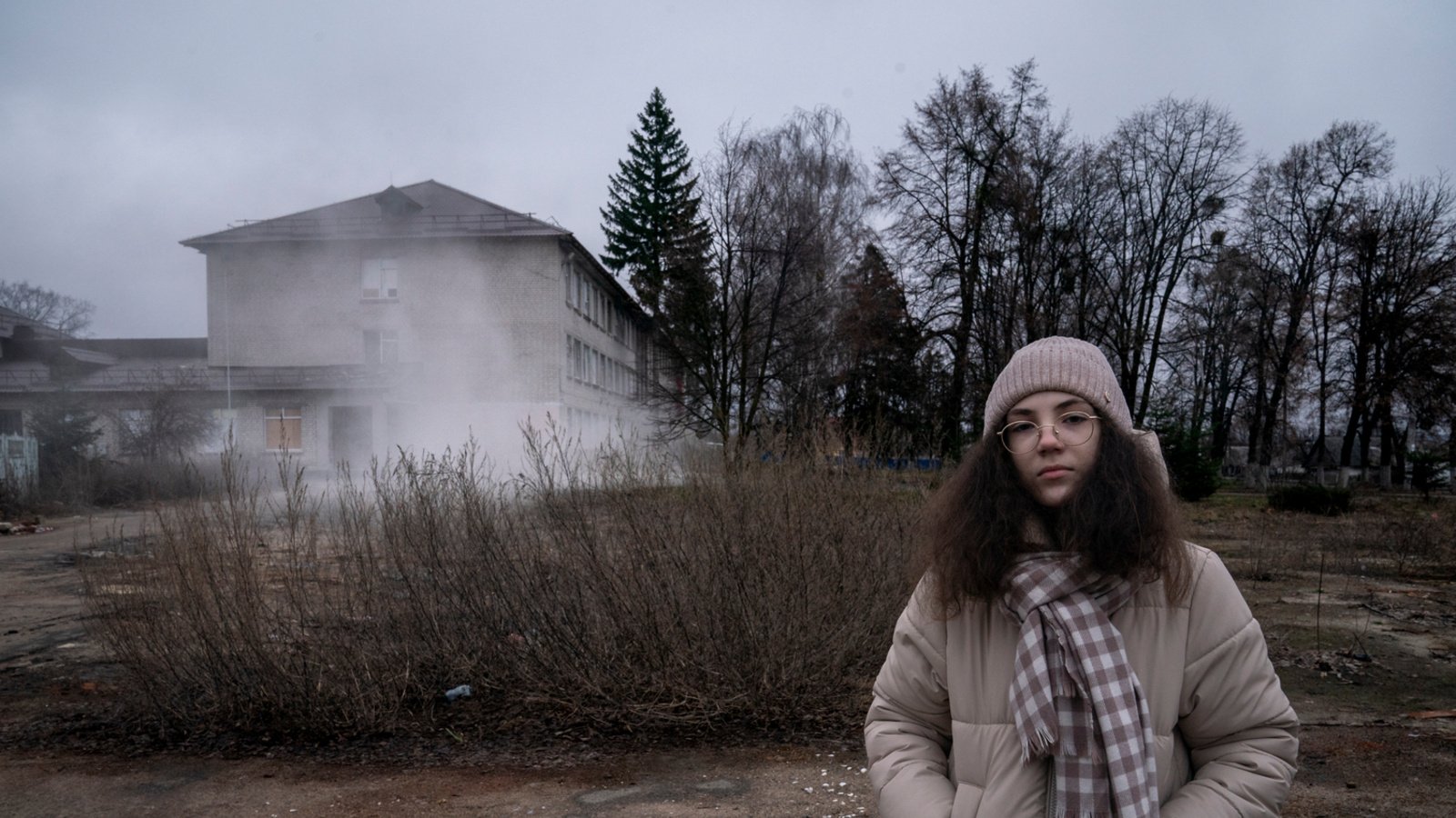 A girl stands in front of a damaged school building.