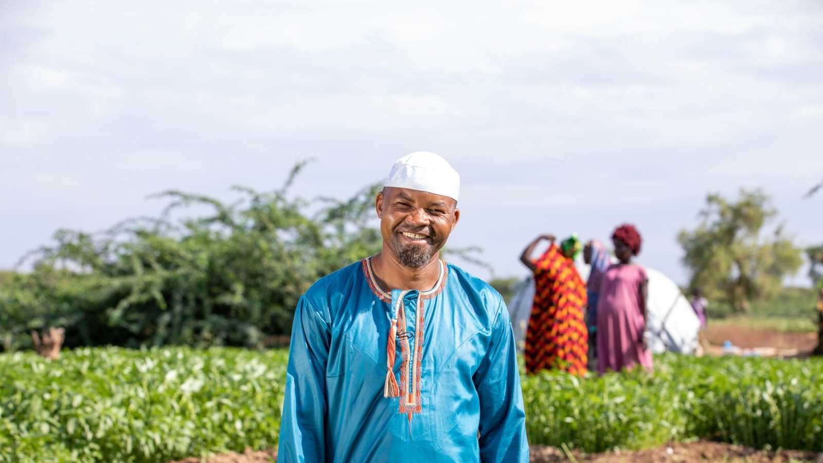 A smiling man stands in a field where crops grow.