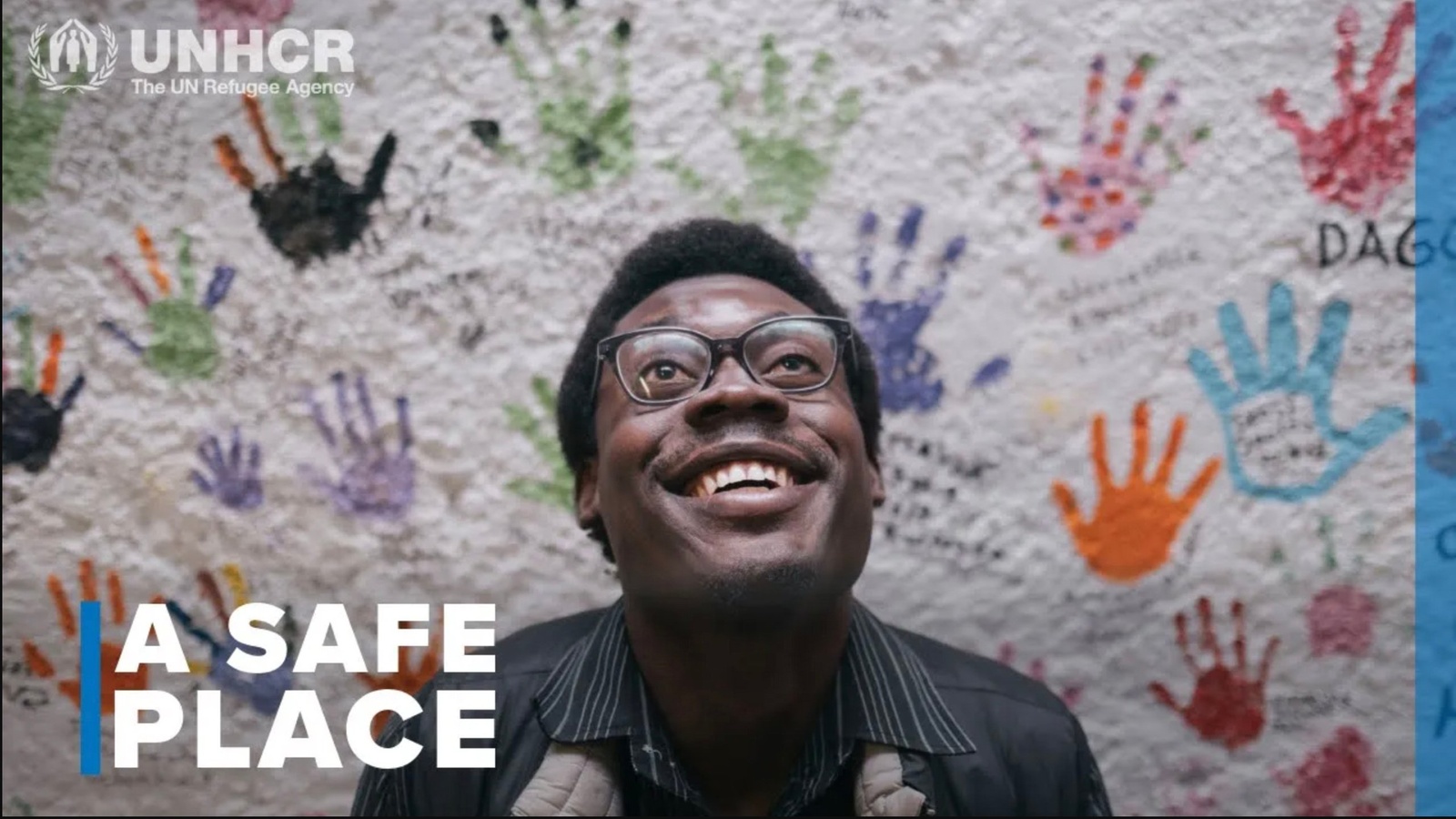A portrait of a man in front of a wall covered in colourful handprints.