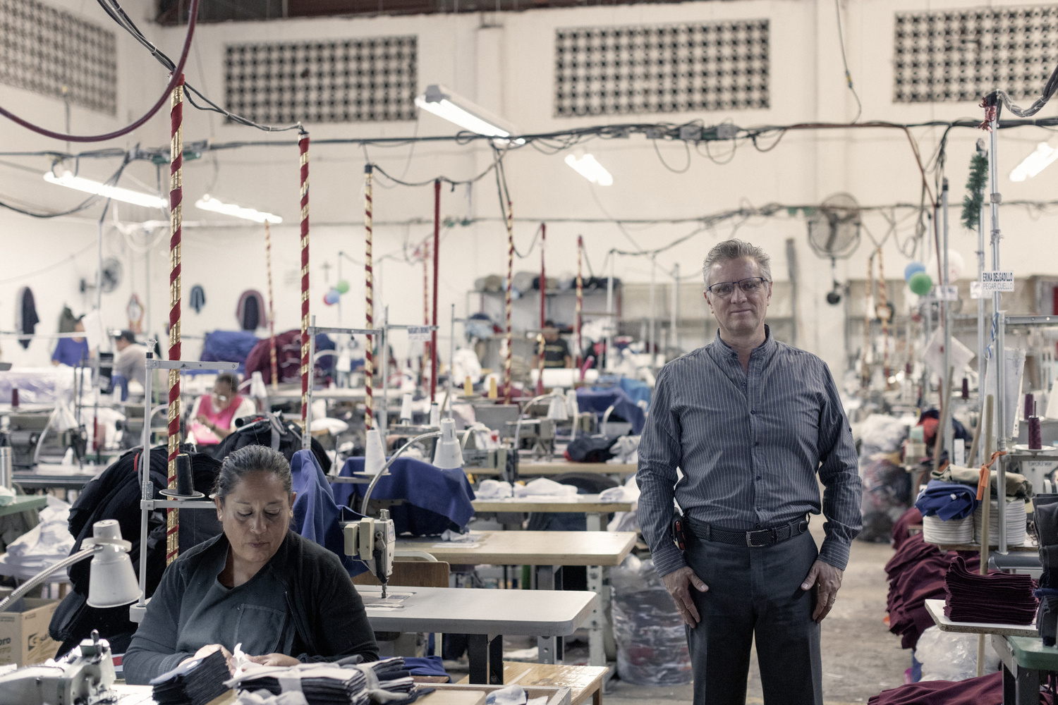 A man stands on a factory floor where women are at work using sewing machines.