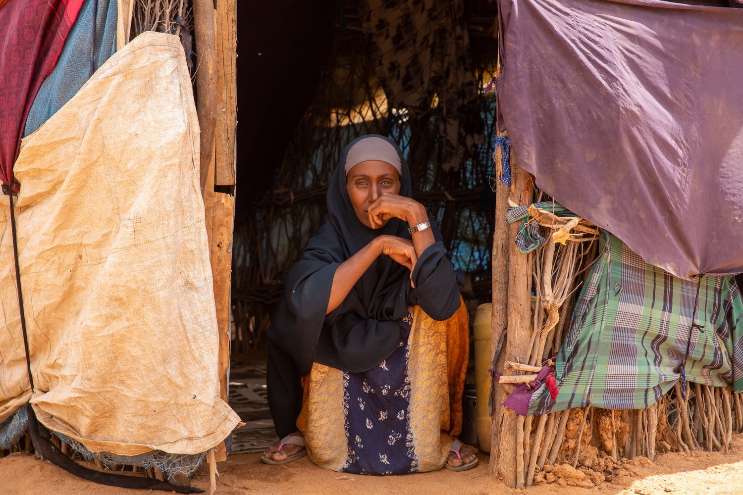 A woman sits at the entrance to a makeshift shelter.