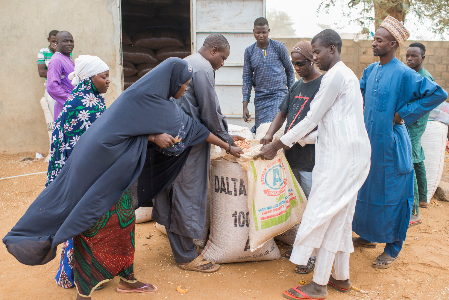 A man transfers groundnuts from a large sack into a smaller bag while others look on.