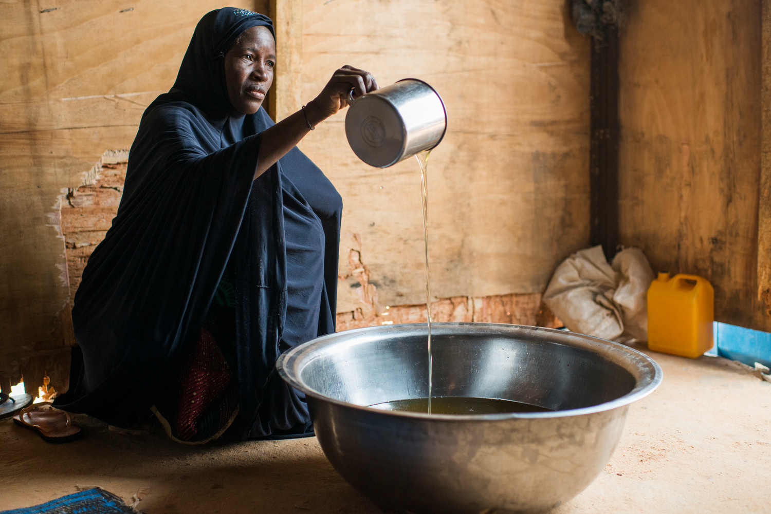 A woman pours oil into a large metal bowl.