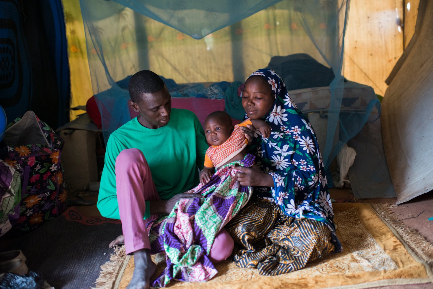A man and a woman sit on a mat holding a small child.
