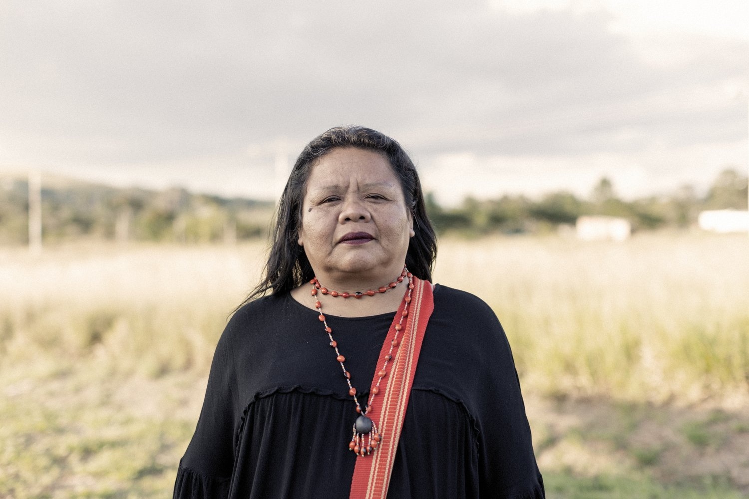 Portrait of a woman wearing a black shirt with a red sash and beaded necklace