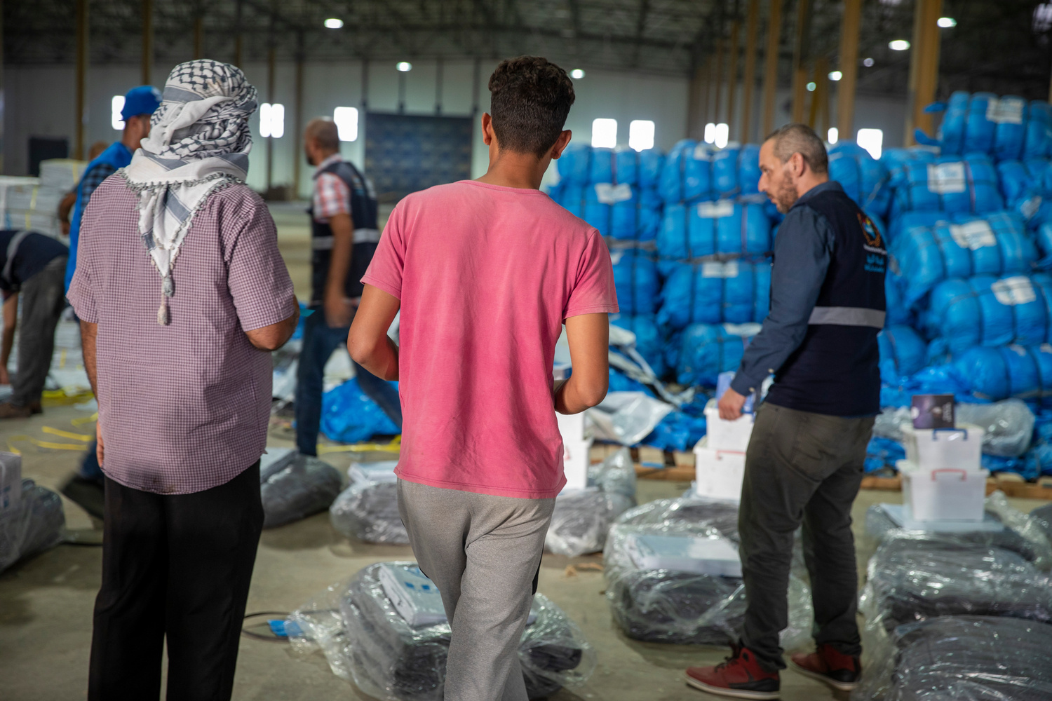 Two men wait to receive blankets from aid workers in a warehouse.