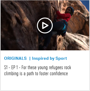 young woman in red shirt and blue leggings climbs the side of a brown rock face