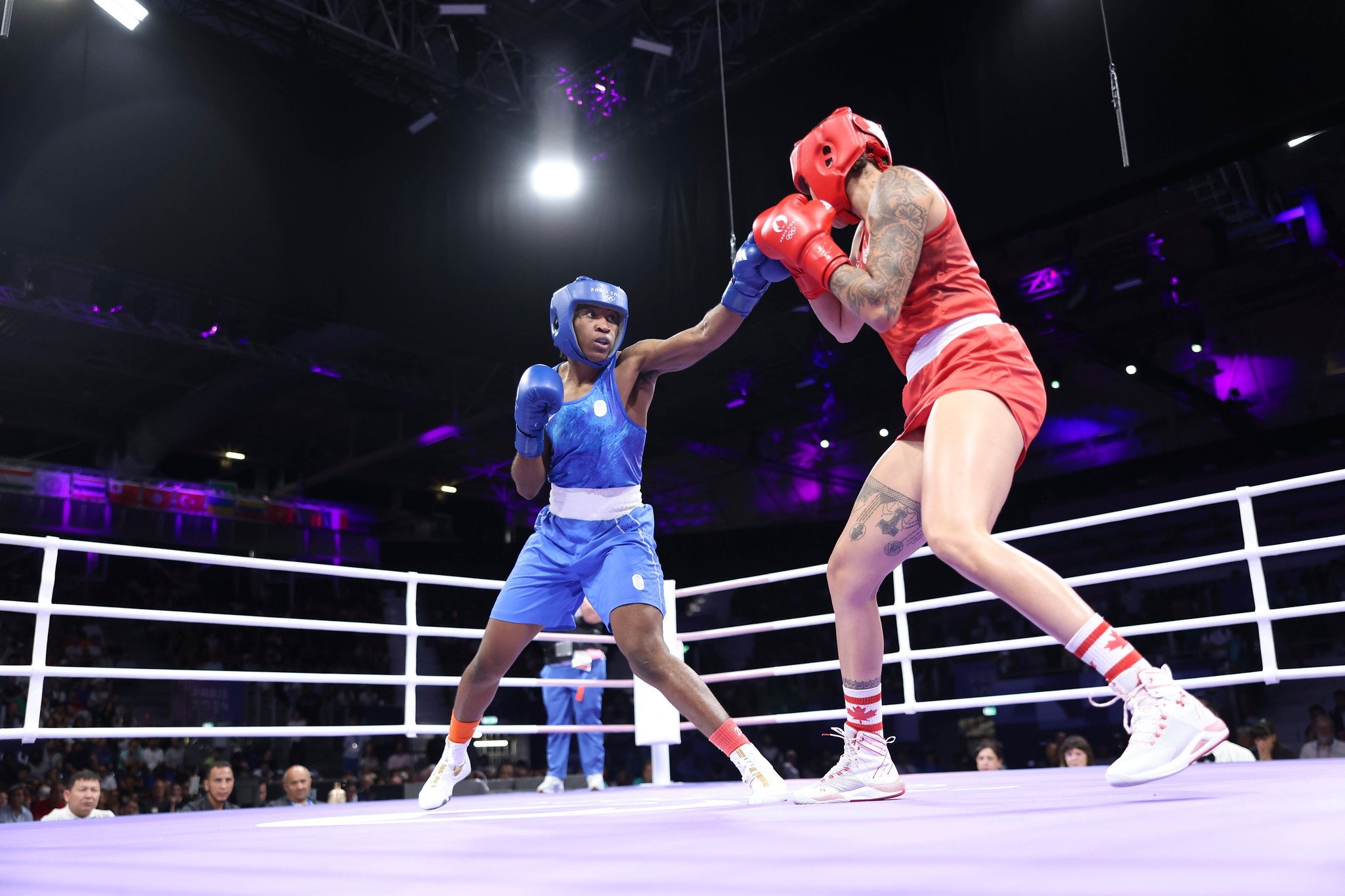 A woman dressed in blue fights with a woman dressed in red in a boxing ring.
