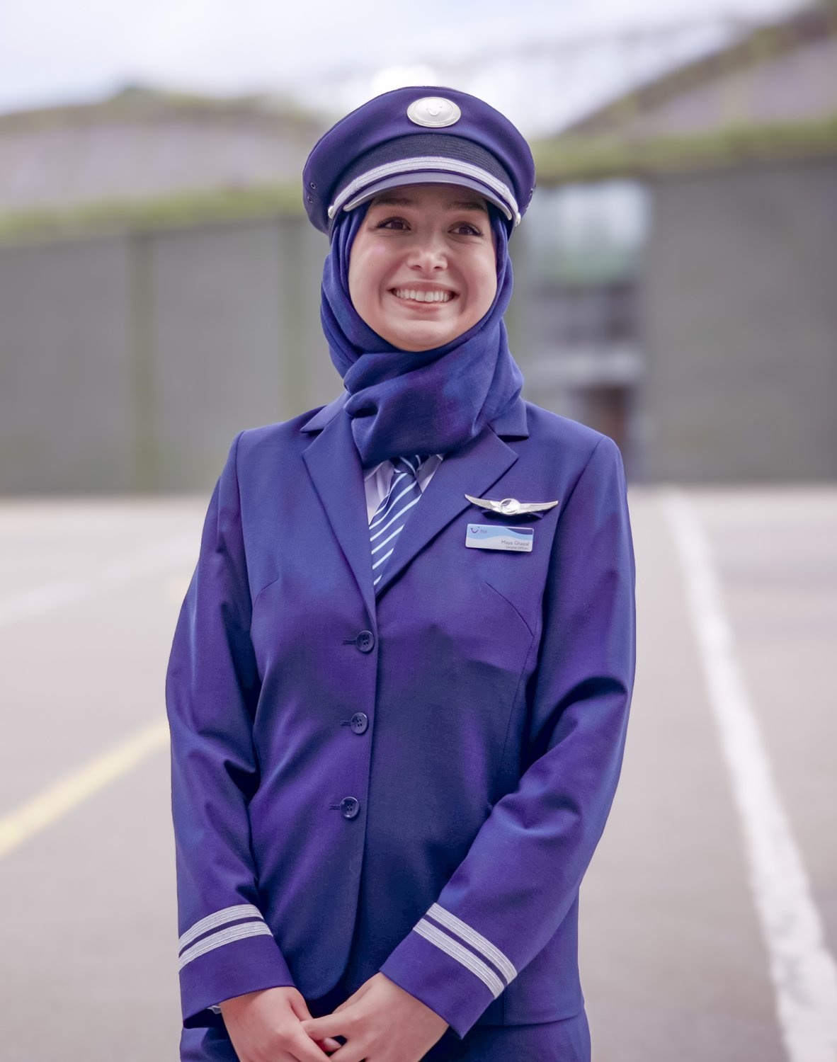 A woman in a purple pilot's uniform stands outside an aircraft hangar