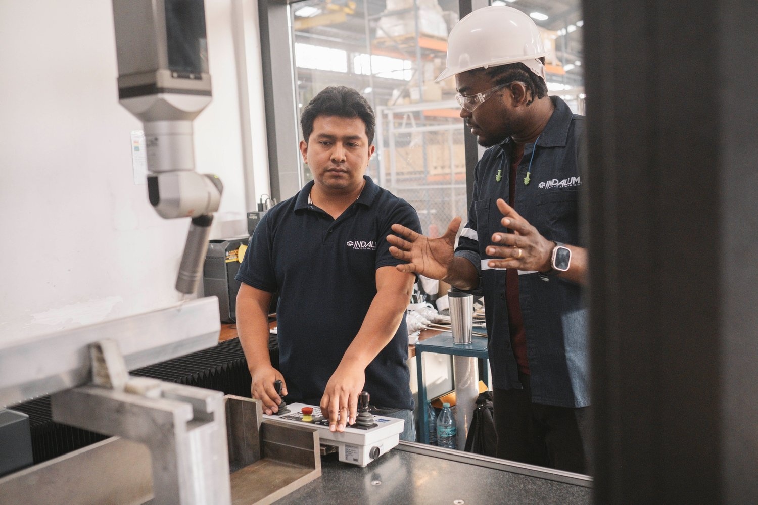 A man in a hard hat talks to a colleague operating machinery in a factory