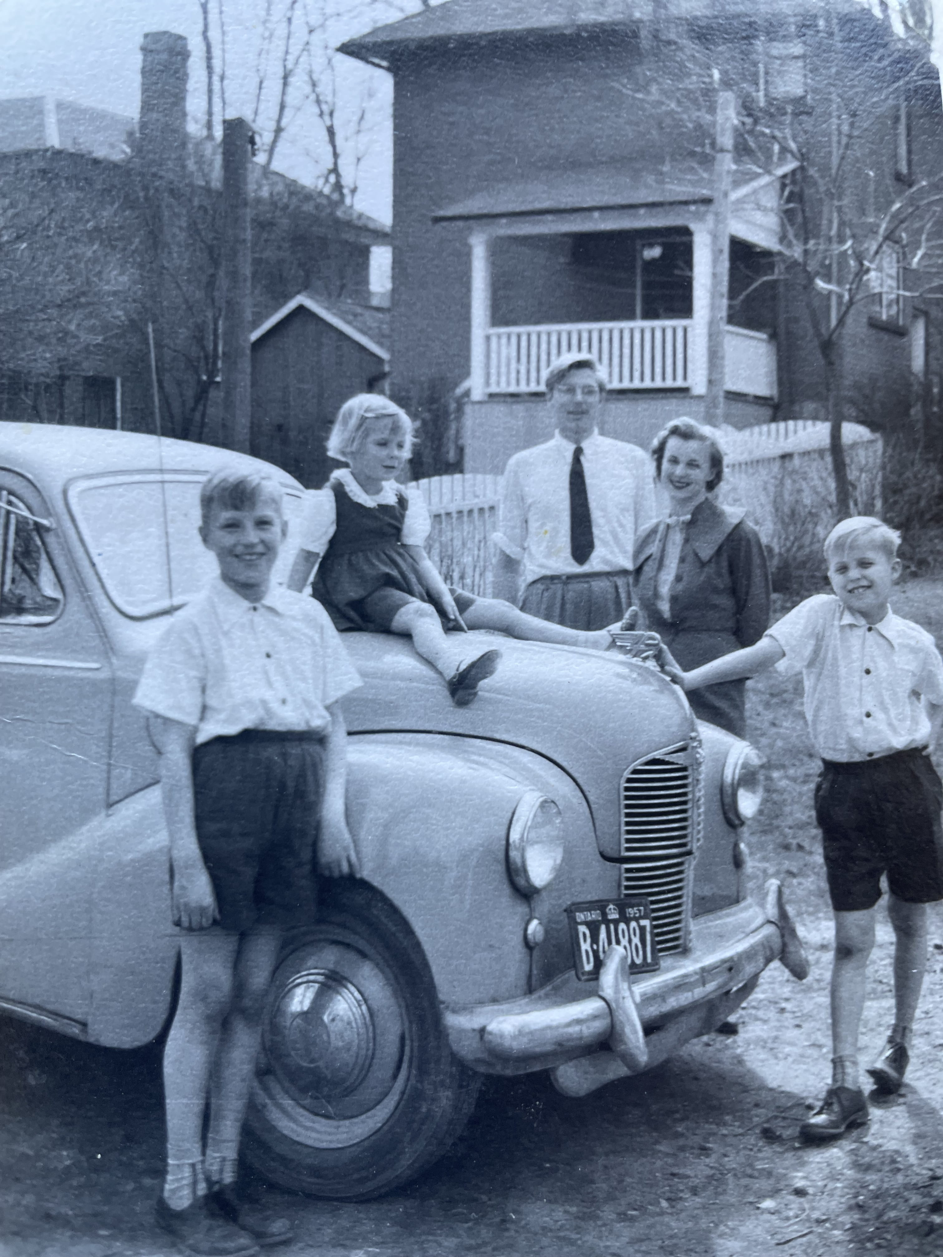 A family poses for a black-and-white photo around an old-fashioned car parked outside a house