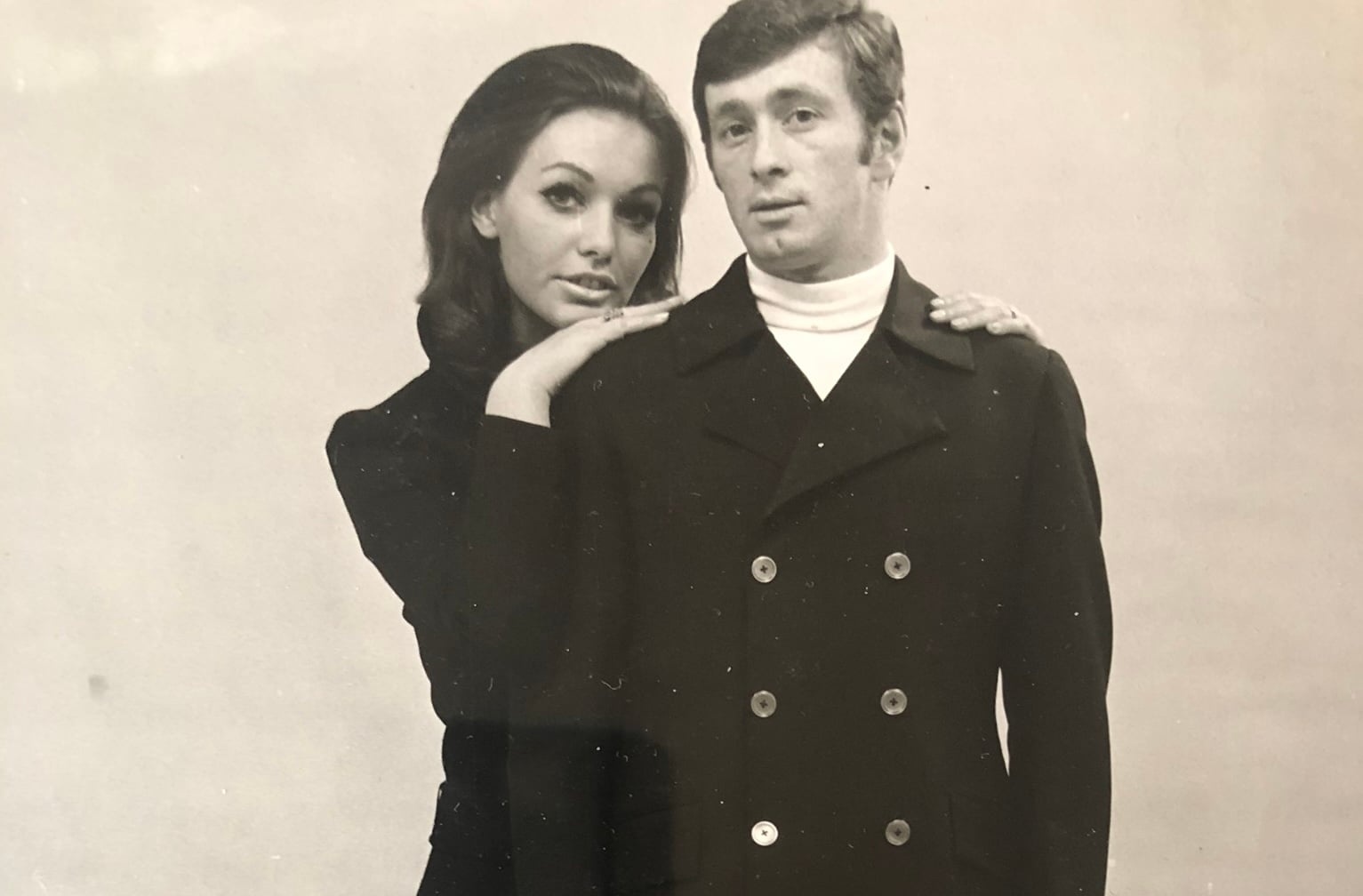 A man and a woman in 1960s clothing pose together in a sepia faded image
