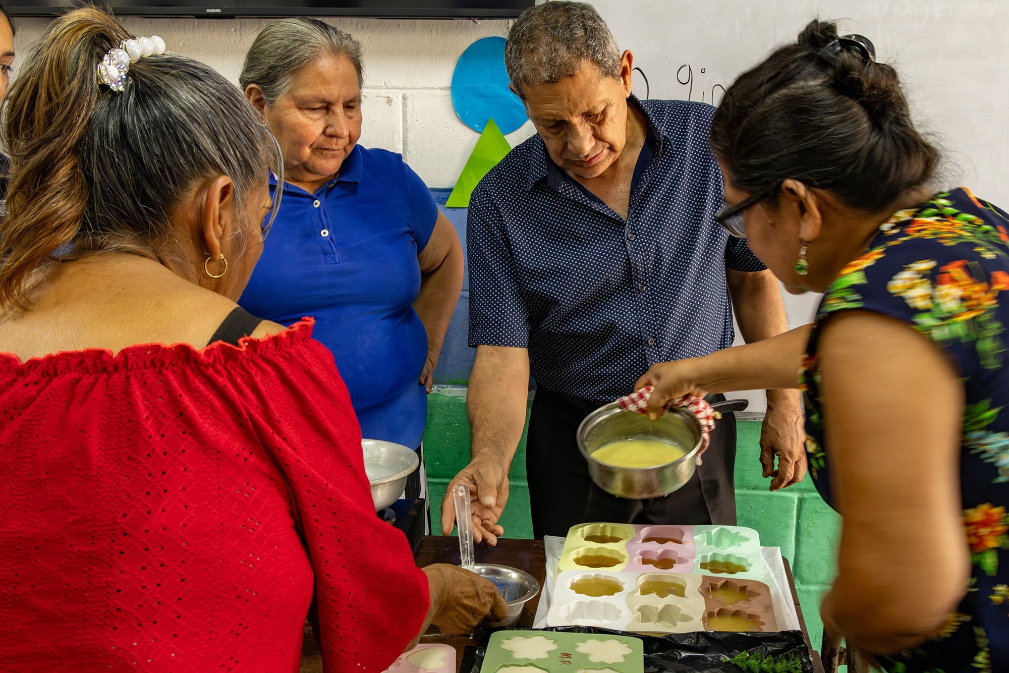 Un hombre mayor al centro y tres mujeres a su alrededor forman un grupo para preparar jabones
