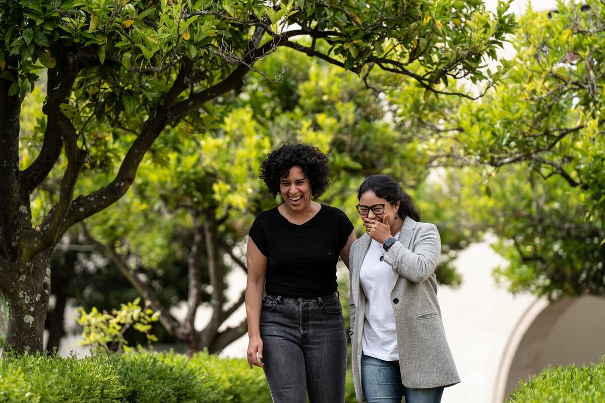 Two women share a joke as they walk through a park.