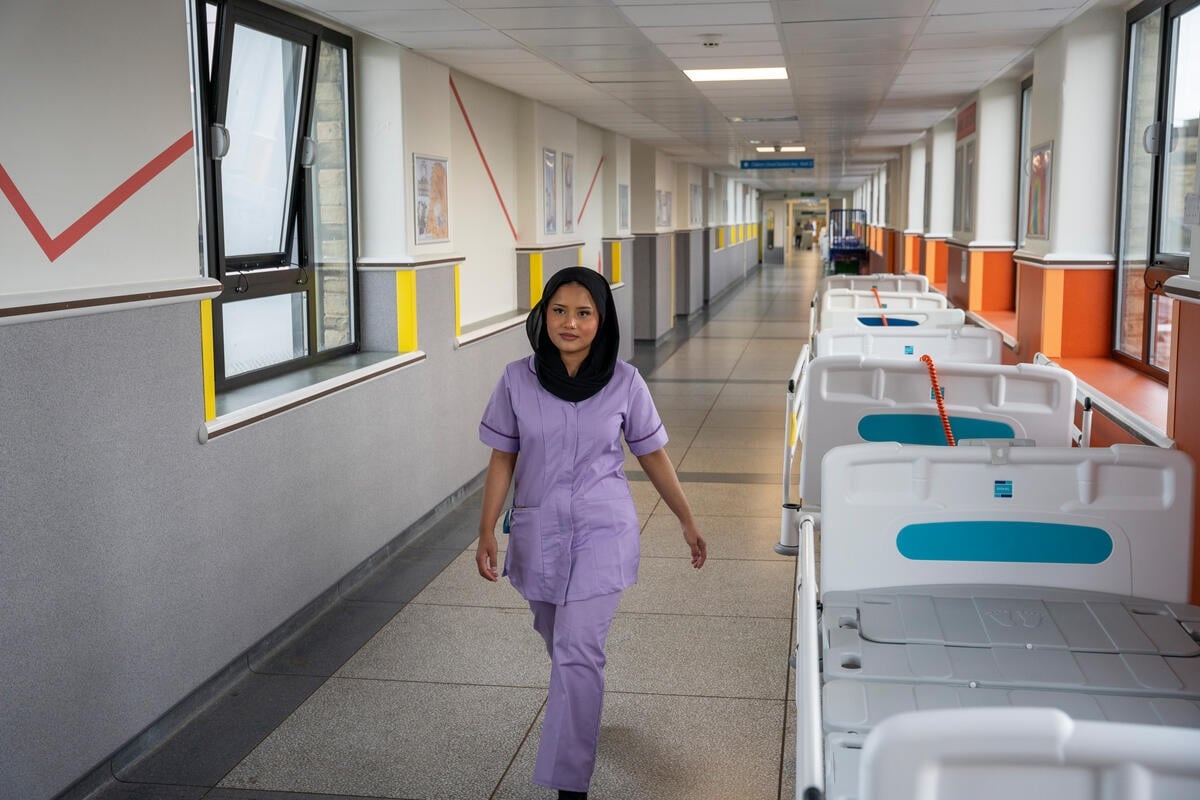 A woman wearing a nurse's outfit walks in the hallway of an hospital.