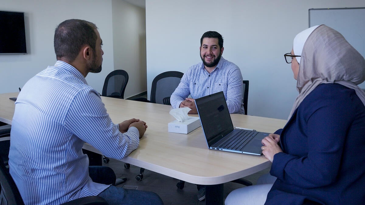 Zeina Hyari meets with Ziad and another Syrian refugee in a meeting room