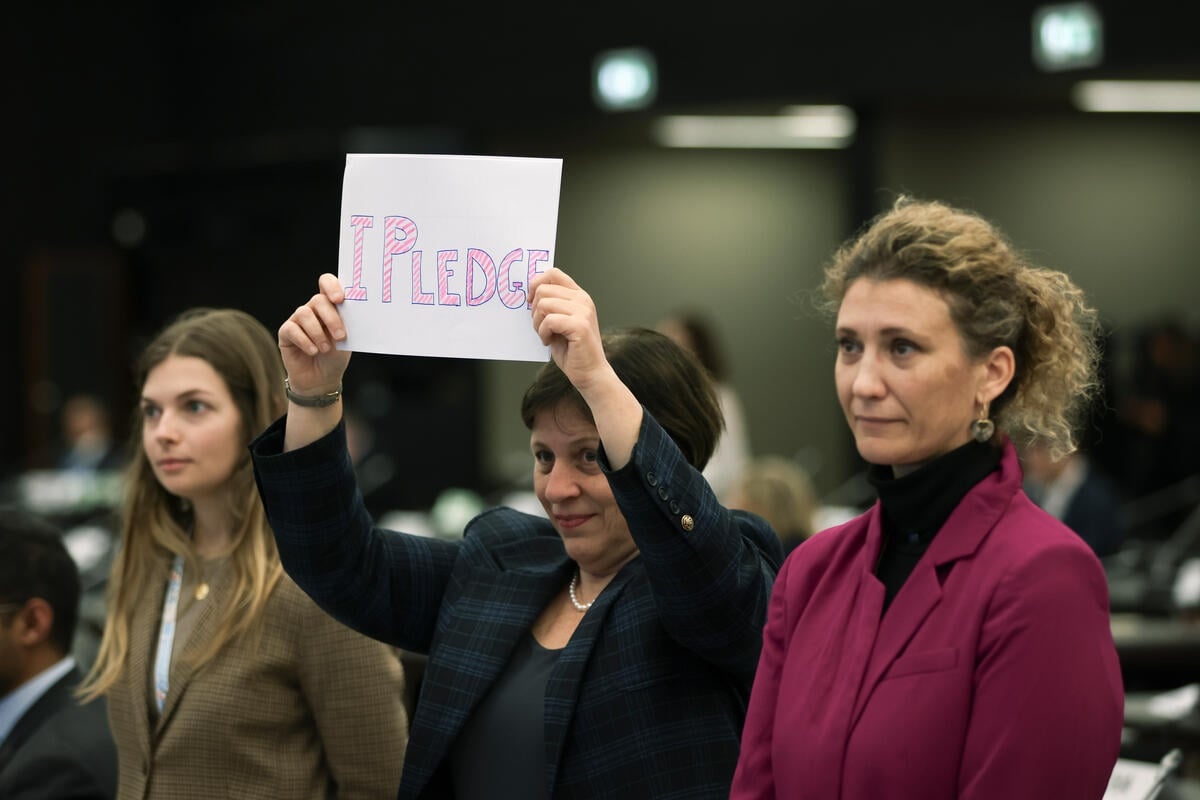 Three individuals stand together, one holds up a sign that reads 'I pledge'.