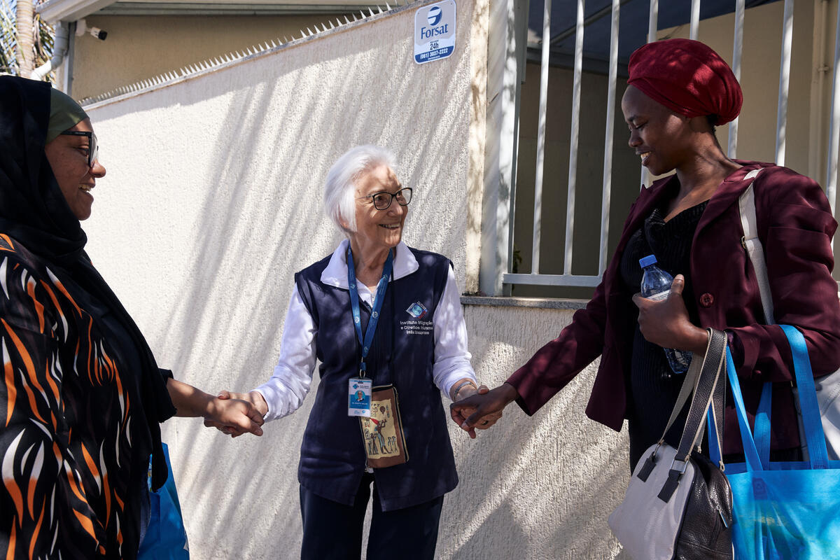 Three smiling women hold hands outside a building