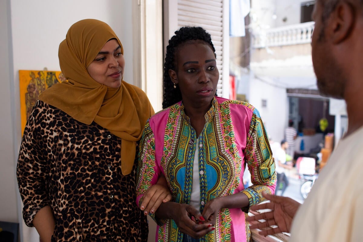 Two women link arms and listen to a man talking.