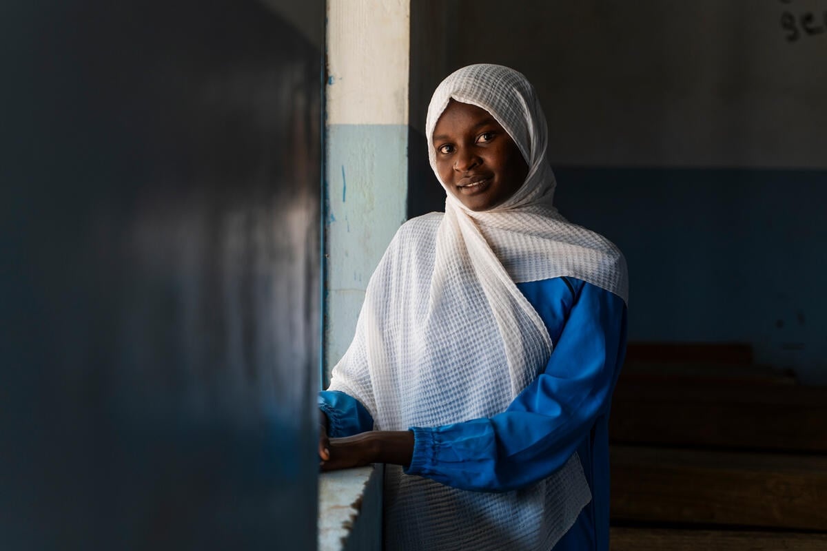 A portrait of a young woman wearing a white headscarf leaning on a window sill.