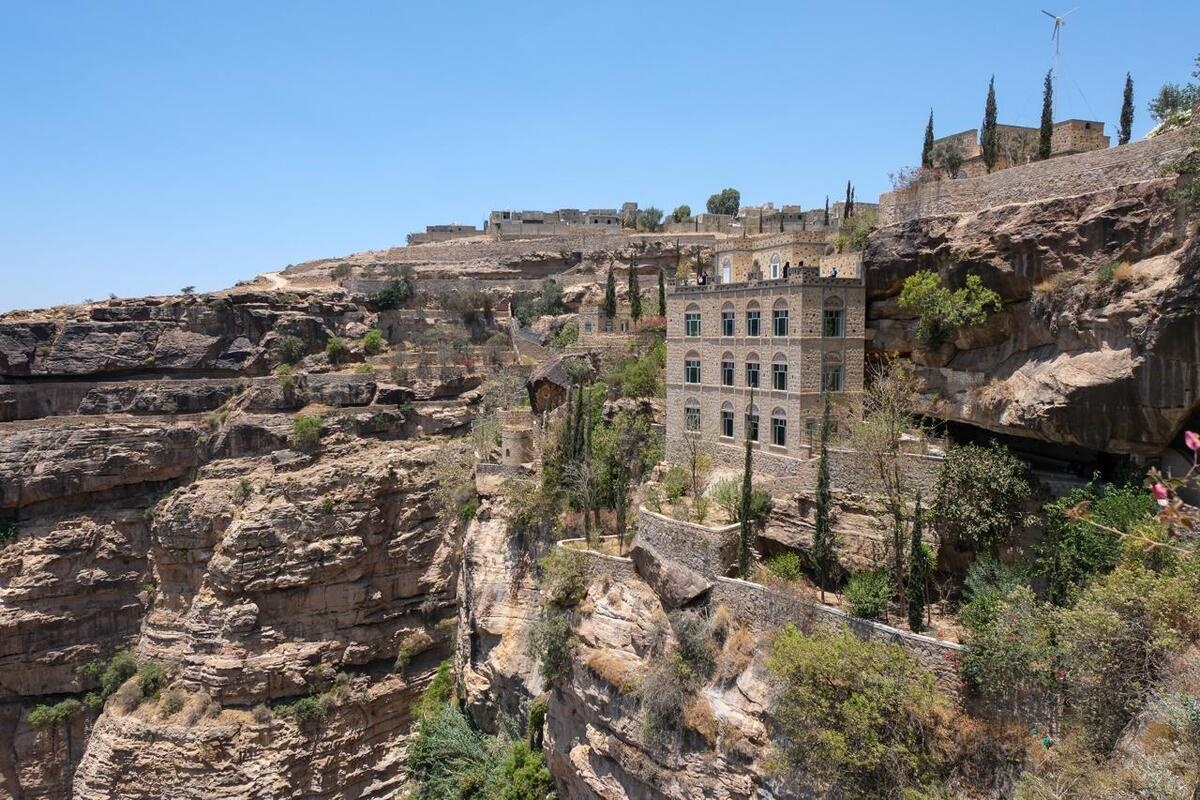A four-storey building surrounded by trees is perched at the top of a rocky cliff.