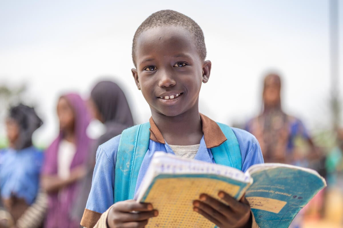 A young boy wearing a backpack and holding an open class exercise book