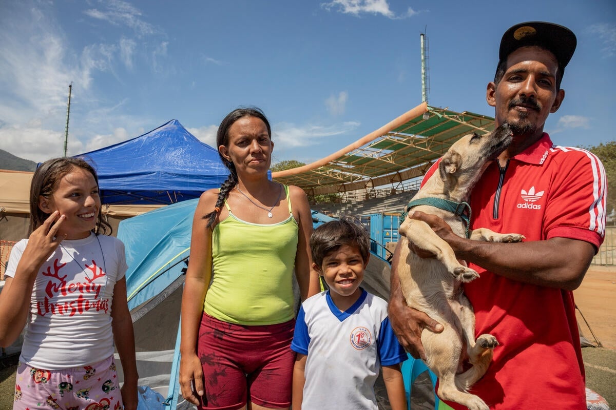 A woman and two children stand outside a tent next to a man holding a dog