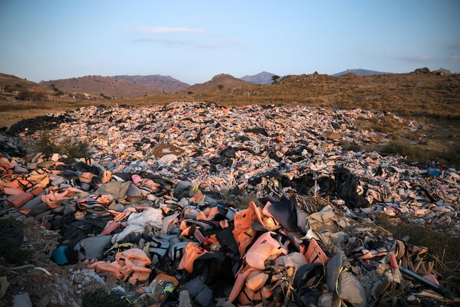 A large pile of discarded orange lifejackets lies in a field.