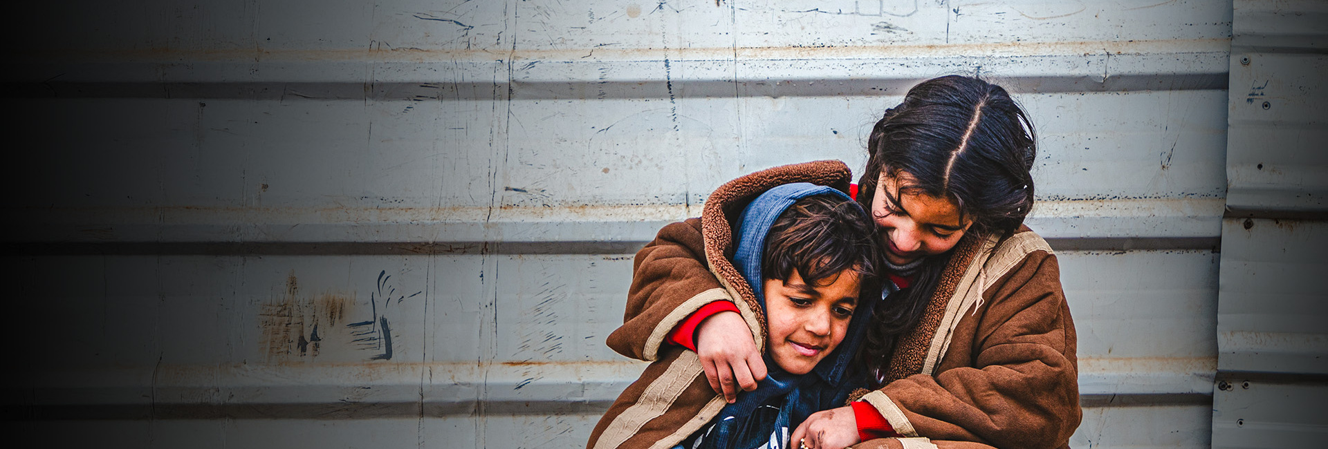 A young Syrian refugee wraps herself and her younger brother in a blanket as they sit outside in the cold in the Zaatari refugee camp.