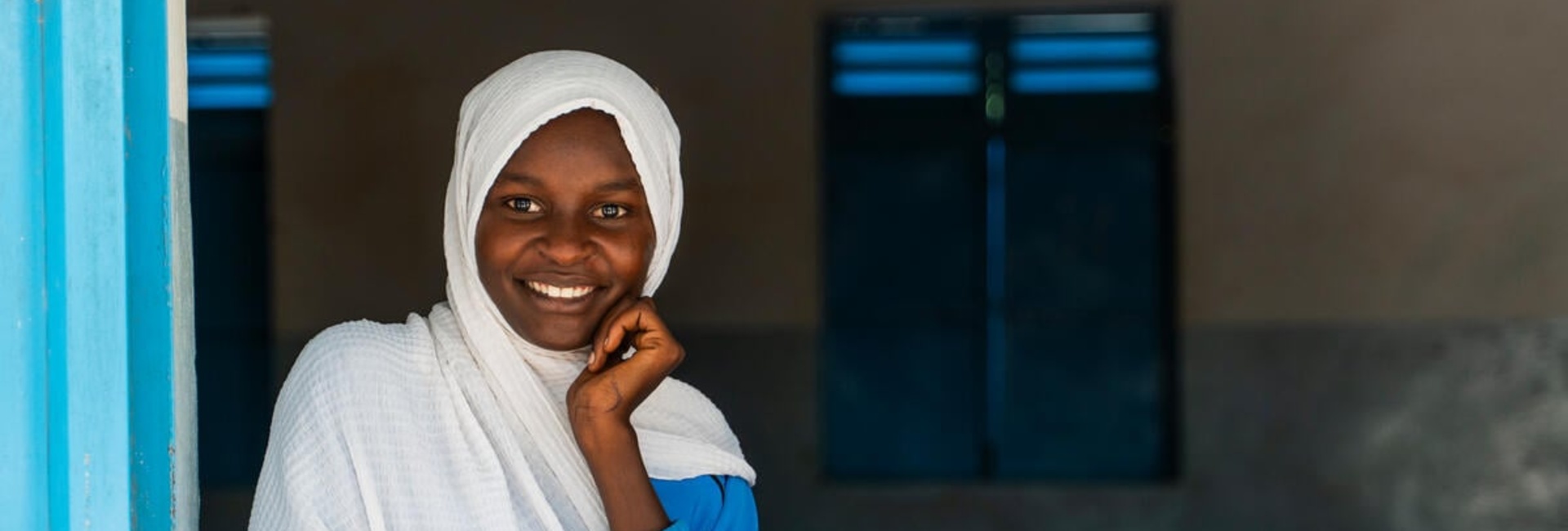 A young girl smiles at the camera, looking through an open window.