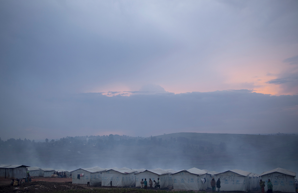 People stand near a row of white tents on a hillside at dusk.